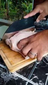 Person cutting raw chicken on wooden board.