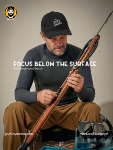 Man assembling spearfishing gear, focus below surface.