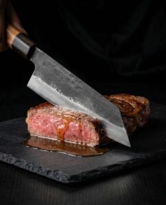 Chef slicing juicy steak on slate board.