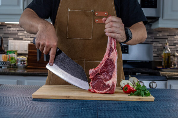 Person slicing raw meat on cutting board in kitchen.