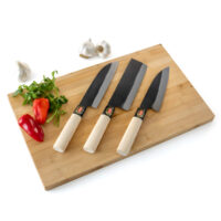 Three kitchen knives on wooden cutting board with vegetables.