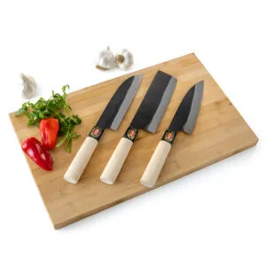 Three kitchen knives on wooden cutting board with vegetables.