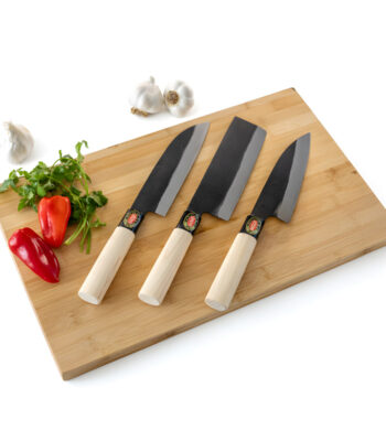 Three kitchen knives on wooden cutting board with vegetables.