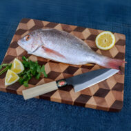 Fresh fish with knife, herbs, lemons on board.