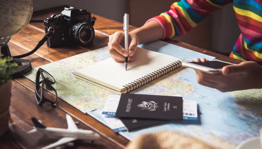 Person planning travel with map, notebook, and phone.