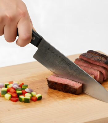 Slicing steak on cutting board with vegetables.