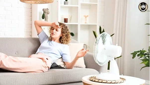 Woman on couch cooling off with fan indoors.