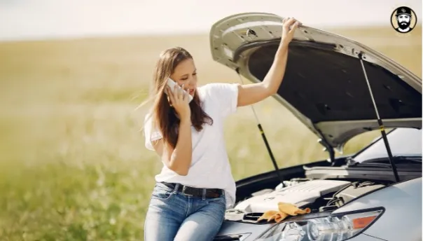 Woman calling for help beside a broken-down car with the hood open.