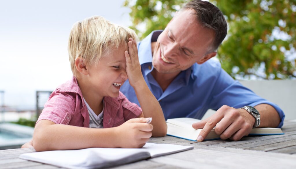 Father and son laughing over homework outdoors.