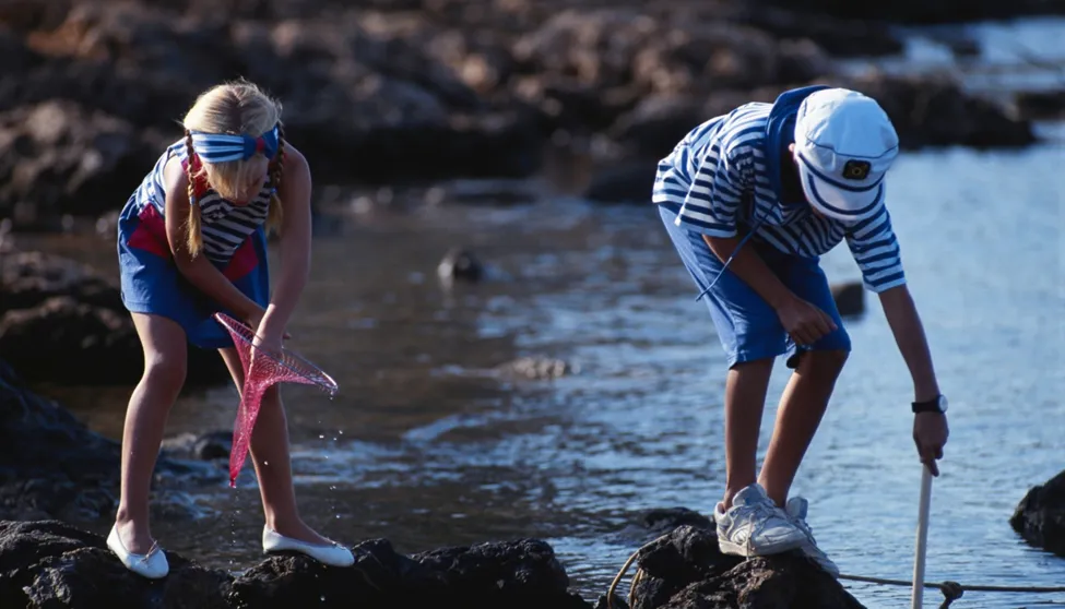 Children exploring rocks near water in summer.