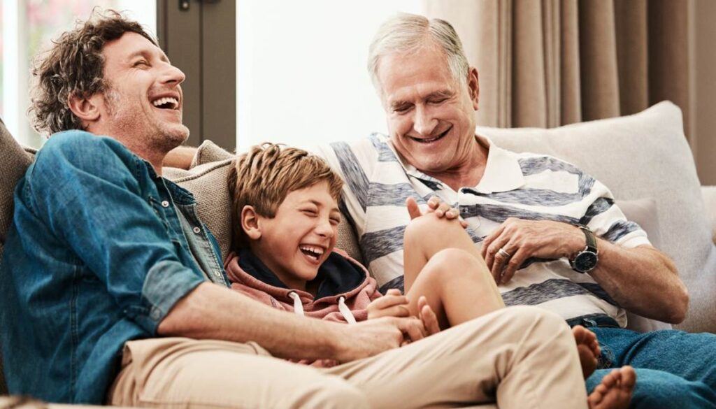 Three generations laughing together on a couch.