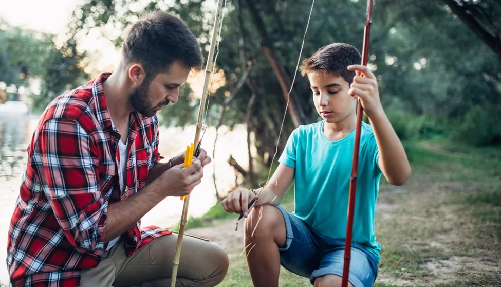 Man teaching boy how to fish by river.