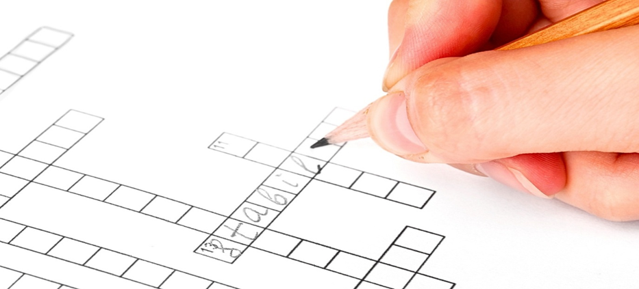 Hand filling out crossword puzzle with pencil.