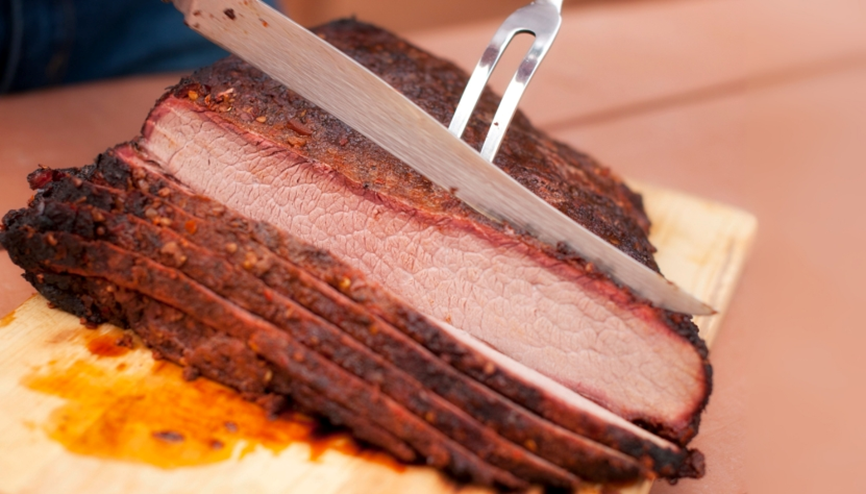 Sliced smoked brisket being carved on a wooden cutting board.

