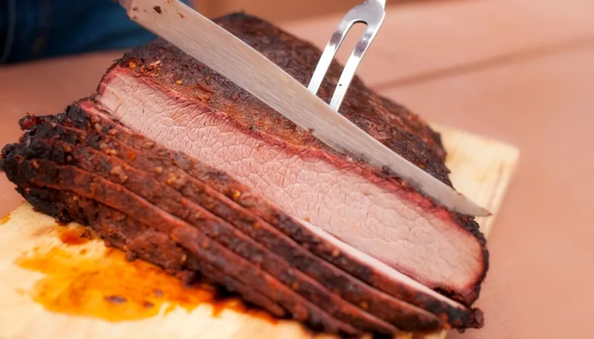 Sliced smoked brisket being carved on a wooden cutting board.

