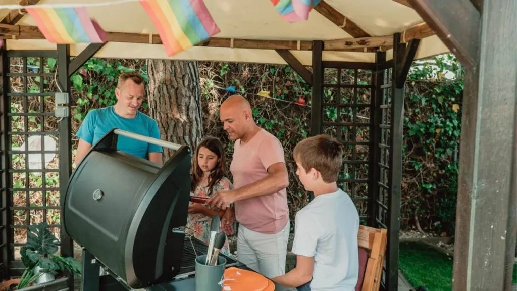 Family barbecue under gazebo with rainbow flags.