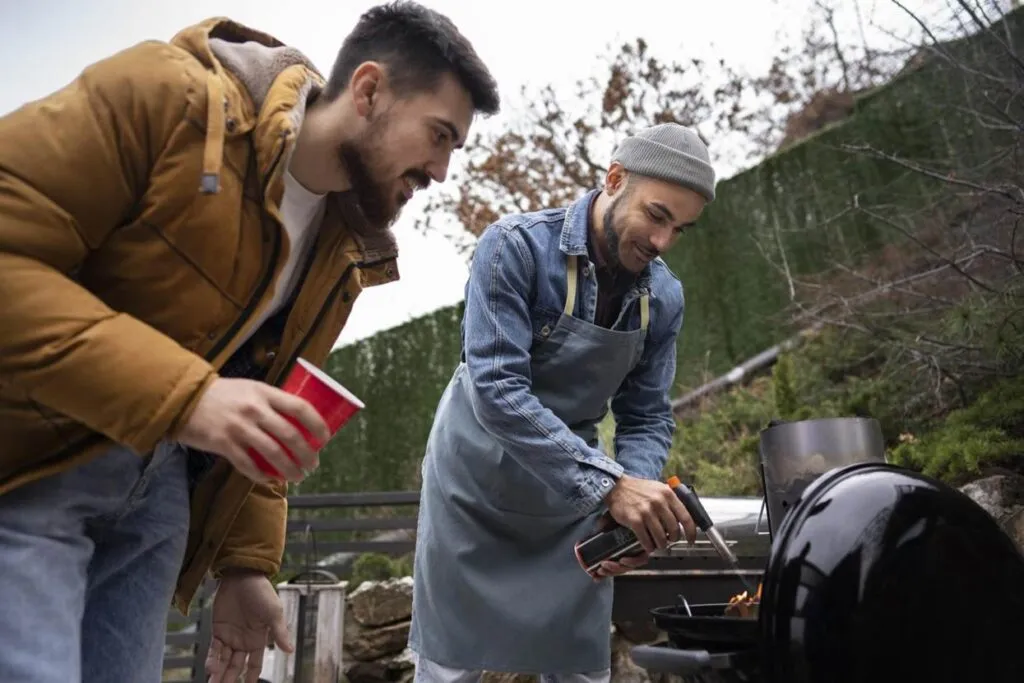 Two men grilling outdoors, one using a torch.
