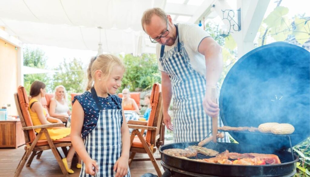 Father and daughter grilling at outdoor family barbecue.