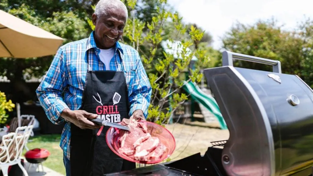 Man grilling meat outdoors, wearing Grill Master apron.