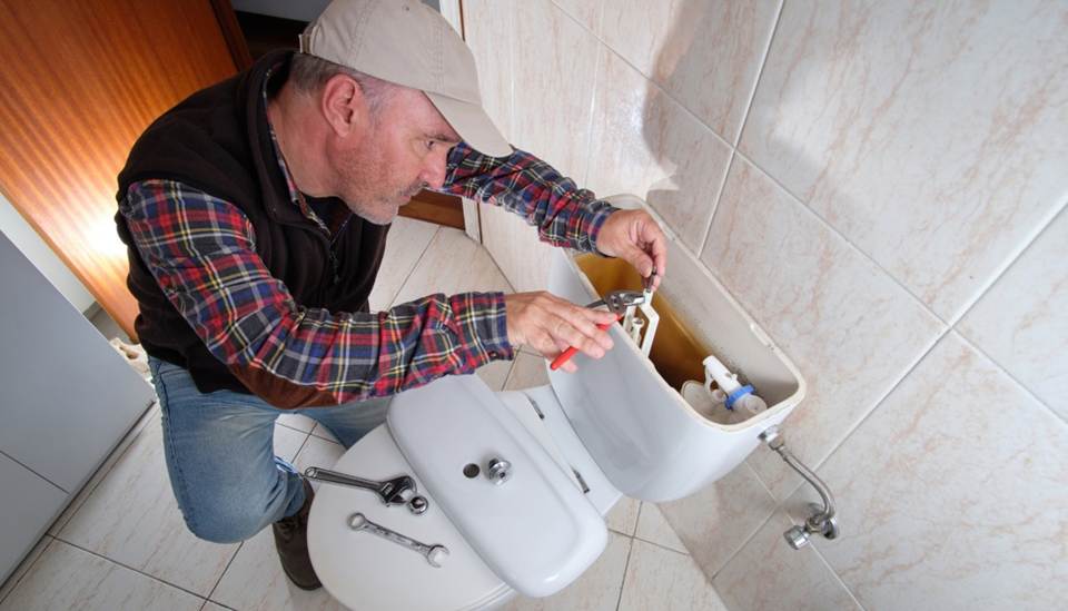 Plumber repairing toilet tank with tools