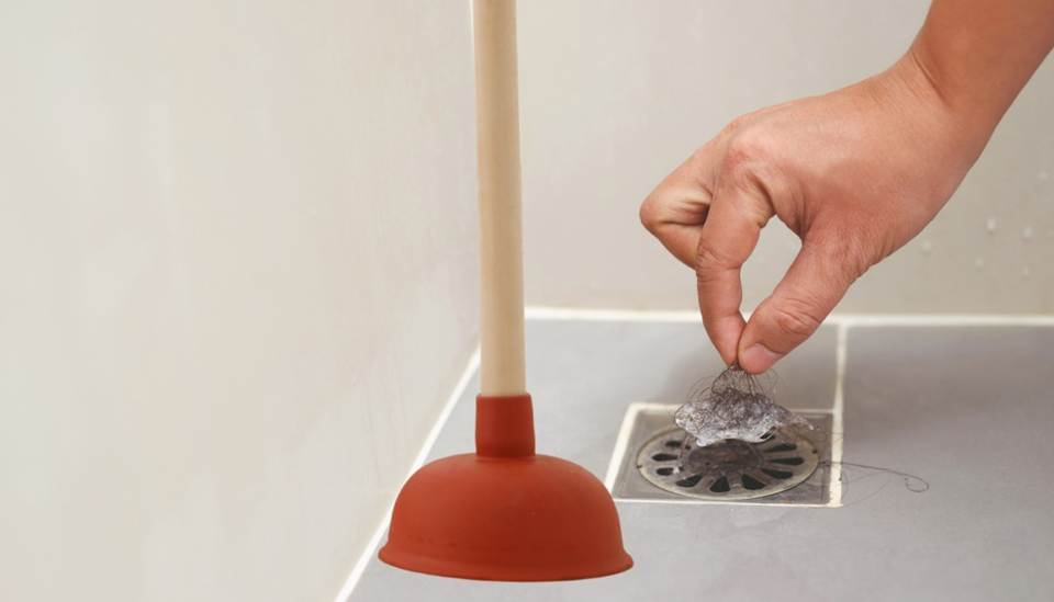 Cleaning hair from shower drain with plunger nearby.