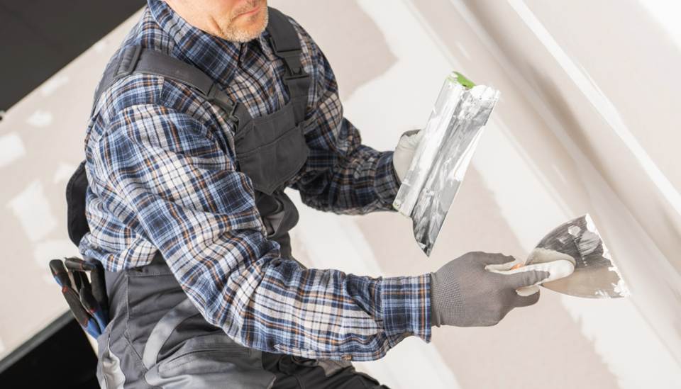 Construction worker smoothing drywall on wall.