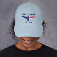 Woman wearing a light blue veterans cap.