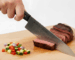 Slicing steak with chef knife on cutting board.