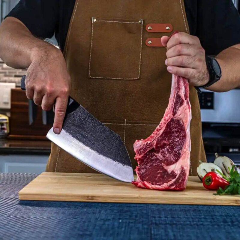 Chef cutting raw tomahawk steak with cleaver.