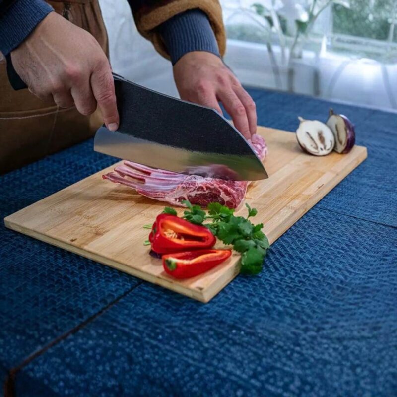 Slicing lamb rack on cutting board with vegetables.