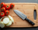 Top-down view of a chef’s knife on a cutting board with sliced onions and tomatoes.