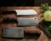 Chinese vegetable cleaver, Western meat cleaver, and heavy bone cleaver laid in a row on a walnut butcher block