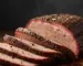 Sliced smoked brisket with smoke ring and pepper bark fanned out on a wooden butcher board