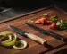 Paring knife with apple peels next to a petty knife with sliced strawberries on a walnut cutting board