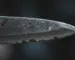 Macro view of a worn chef's knife edge showing micro-chips and dulling under dramatic lighting