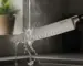Chef's knife being rinsed under running water in a kitchen sink with steam rising