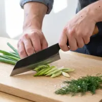 Aogami Bunka Keyaki knife slicing spring onions on an oak board