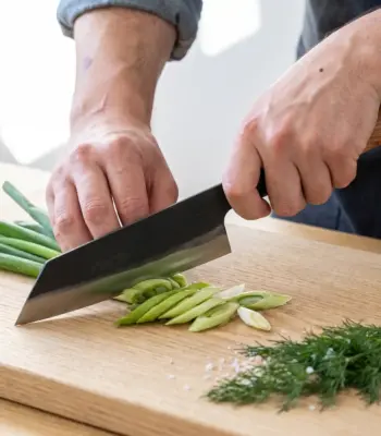 Aogami Bunka Keyaki knife slicing spring onions on an oak board